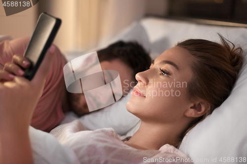 Image of woman using smartphone while boyfriend is sleeping