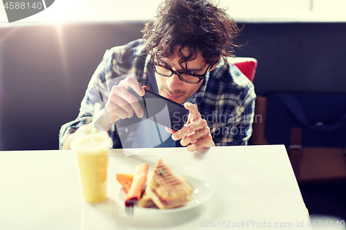 Image of man with smartphone photographing food at cafe