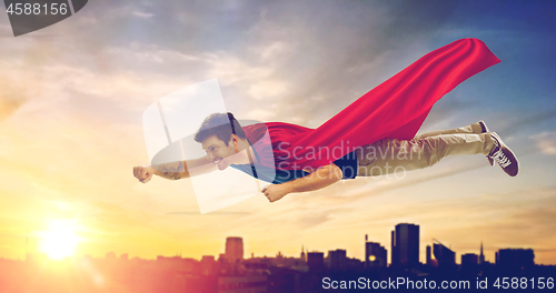 Image of man in superhero cape flying over sunset in city