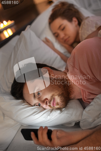 Image of man using smartphone while girlfriend is sleeping