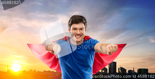 Image of man in red superhero cape over sunset in city