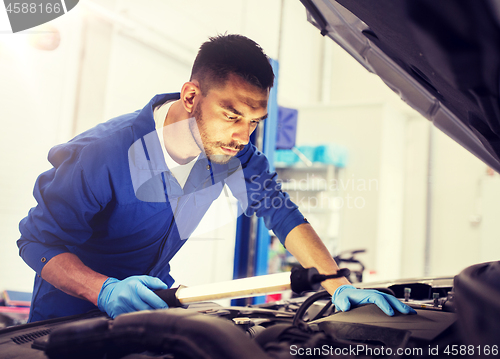 Image of mechanic man with lamp repairing car at workshop