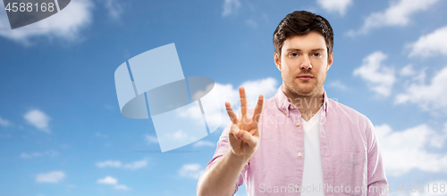 Image of young man showing three fingers over sky