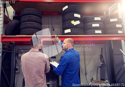 Image of auto mechanic and man with tires at car shop