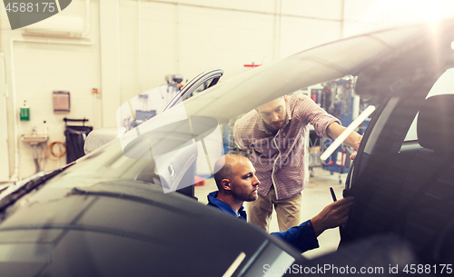 Image of mechanic and man checking seat belt at car shop