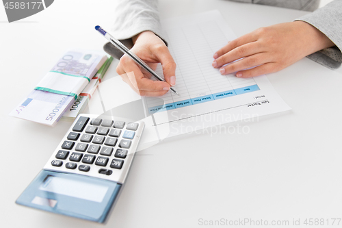 Image of hands with tax form, calculator and money on table