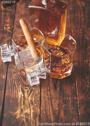 Image of Bottle of whiskey with two glasses and cuban cigar placed on rustic wooden table