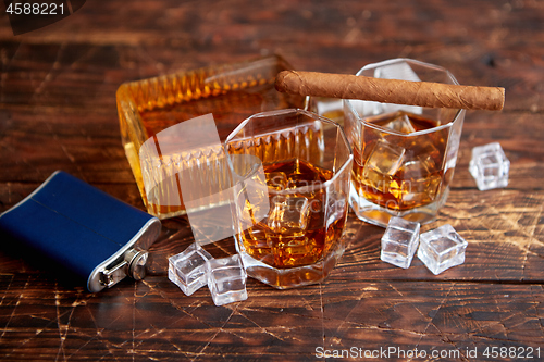 Image of Bottle of whiskey with two glasses and cuban cigar placed on rustic wooden table