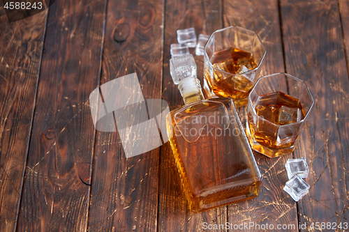 Image of Bottle of whiskey with two glasses placed on rustic wooden table