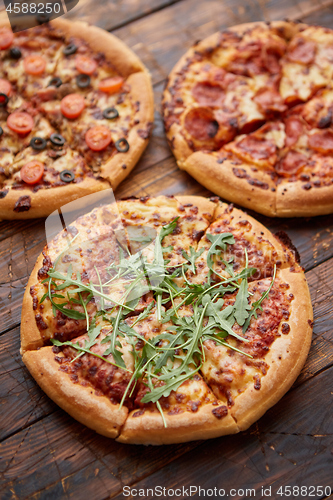 Image of Composition of three various kinds pizzas on wooden table