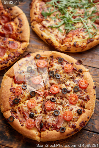 Image of Composition of three various kinds pizzas on wooden table