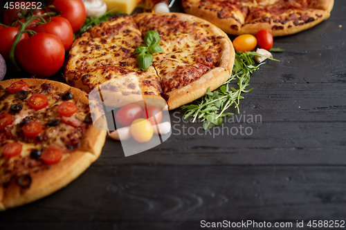 Image of Freshly served, three various pizzas placed among tasty ingredients. Top view