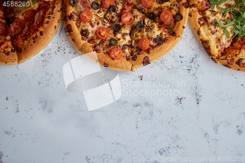 Image of Three different kind of pizzas placed in a row on white rusty ta