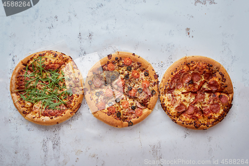 Image of Three different kind of pizzas placed in a row on white rusty ta