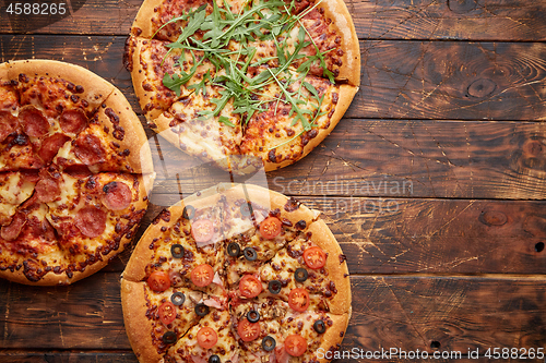 Image of Composition of three various kinds pizzas on wooden table