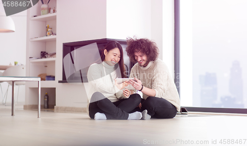 Image of multiethnic couple using tablet computer in front of fireplace