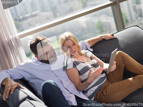 Image of couple relaxing at  home with tablet computers