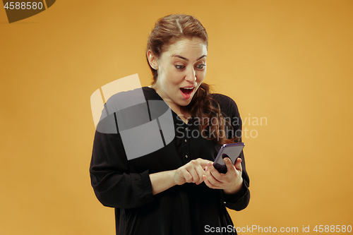 Image of Young beautiful woman using mobile phone studio on gold color background