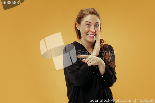 Image of The young woman whispering a secret behind her hand over studio background