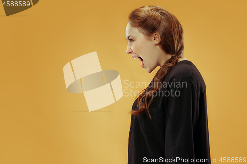 Image of The young emotional angry woman screaming on gold studio background