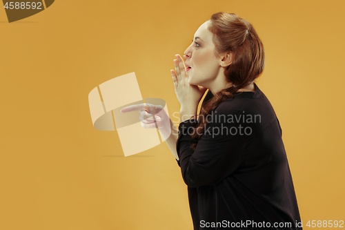 Image of The young woman whispering a secret behind her hand over gold background