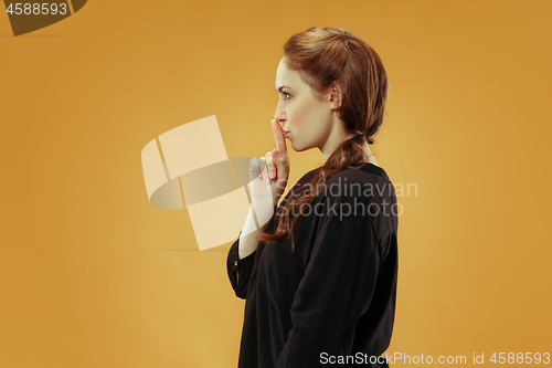 Image of The young woman whispering a secret behind her hand over gold background
