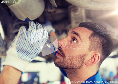 Image of mechanic man with flashlight repairing car at shop