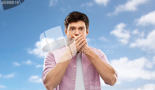 Image of shocked man covering mouth by hands over blue sky