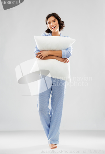 Image of happy young woman in blue pajama hugging pillow