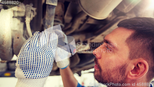 Image of mechanic man with flashlight repairing car at shop