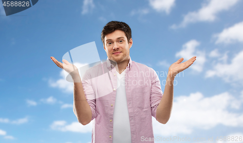 Image of young man shrugging over blue sky background