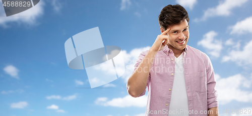 Image of smiling young man pointing finger to his head