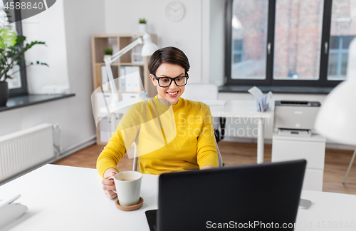 Image of businesswoman with laptop drinks coffee at office