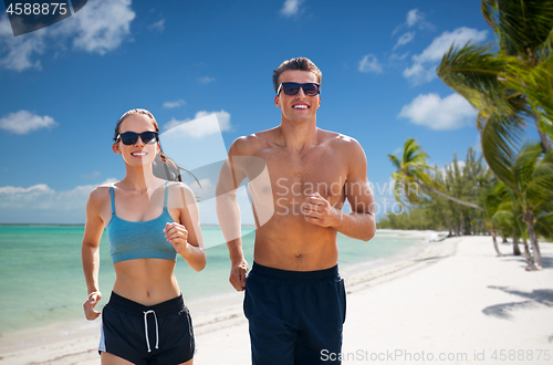 Image of couple in sports clothes running along on beach