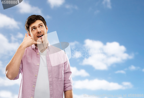 Image of young man showing phone call gesture over blue sky