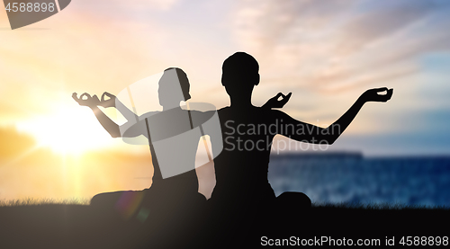 Image of couple doing yoga in lotus pose over sunset