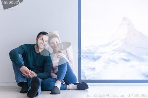 Image of young couple sitting on the floor near window at home