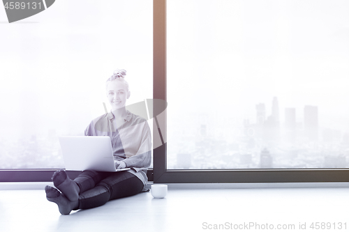 Image of woman drinking coffee and using laptop at home