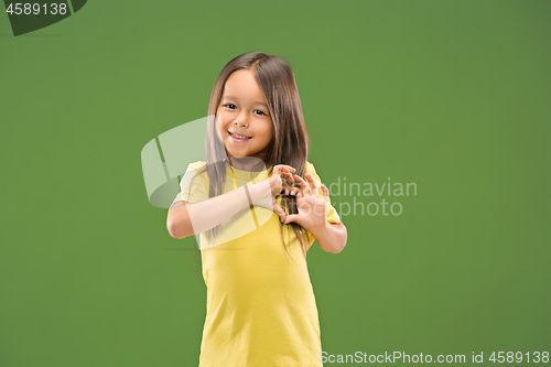 Image of Beautiful smiling teen girl makes the shape of a heart with her hands on the green background.