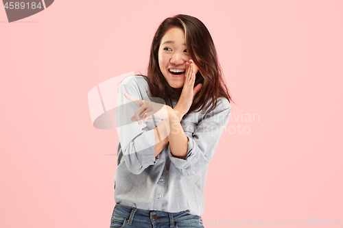 Image of The young woman whispering a secret behind her hand over pink background