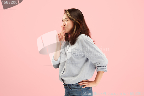 Image of The young woman whispering a secret behind her hand over pink background