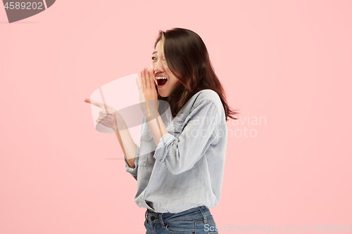 Image of The young woman whispering a secret behind her hand over pink background