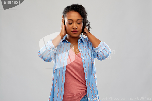 Image of african american woman closing ears by hands