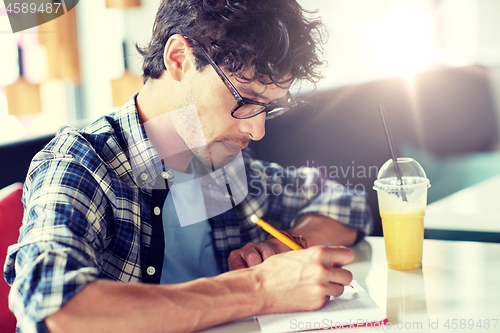 Image of man with notebook and juice writing at cafe