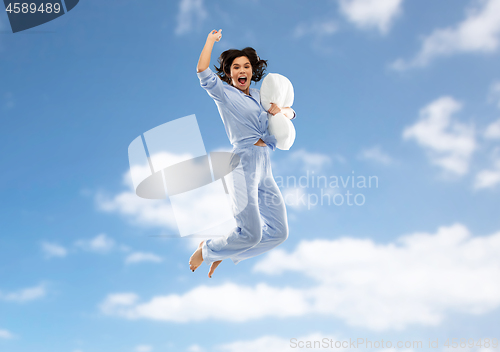 Image of happy woman in pajama jumping with pillow over sky