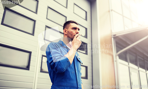 Image of auto mechanic smoking cigarette at car workshop