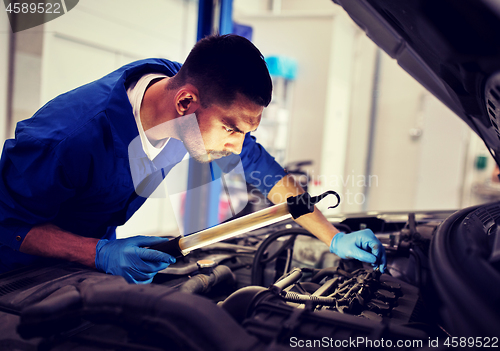 Image of mechanic man with lamp repairing car at workshop