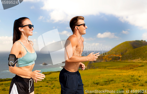 Image of couple with phones and arm bands running on beach