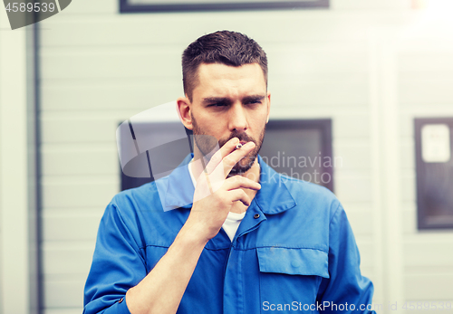 Image of auto mechanic smoking cigarette at car workshop