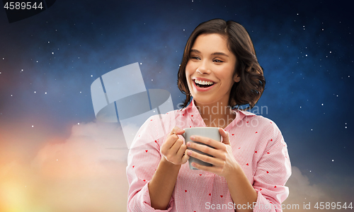 Image of happy woman in pajama with mug of coffee at night